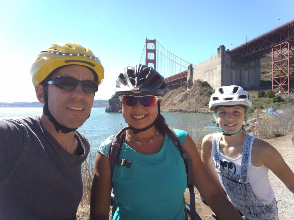three smiling bikers standing in front of the Golden Gate Bridge