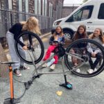 One girl fixing a tire while three other girls watch