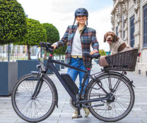 Female with a helmet and plaid shirt with an e-bike and dog in the back basket