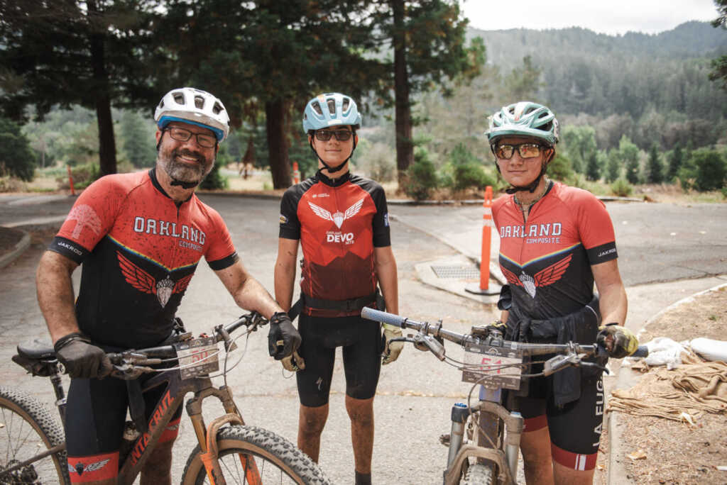three mountain bike riders with bikes and read oakland jerseys