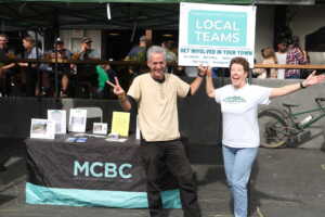 Two volunteers at MCBC's Octoberfest holding "Local Teams" sign