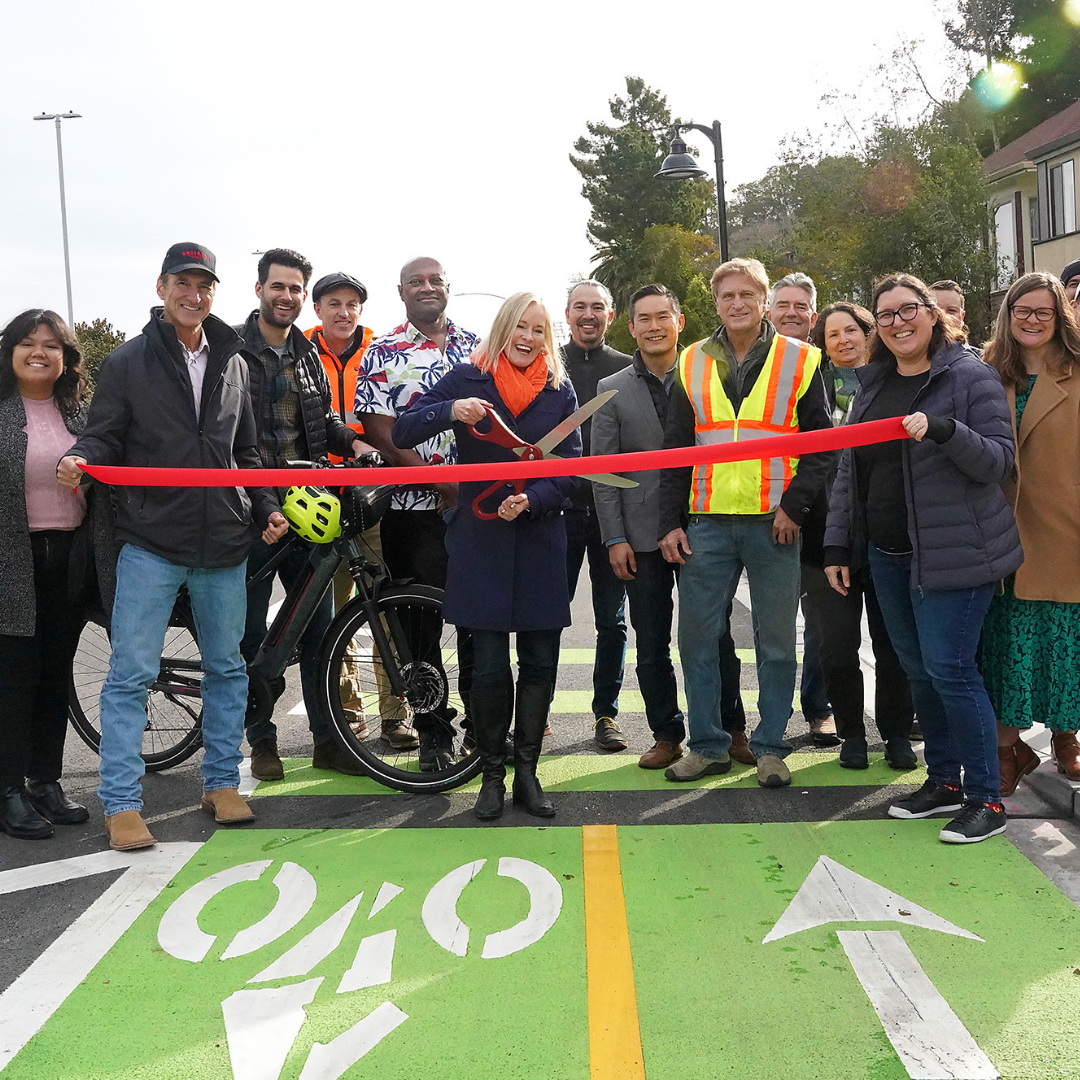 Group of people at 2nd St San Rafael ribbon-cutting ceremony celebrating the opening of a new bike lane, with a woman holding large scissors while others stand smiling behind her