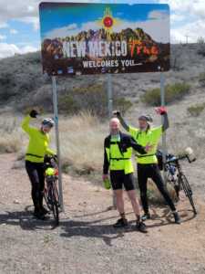 three cyclists in front of new mexico sign - James Bogin trip