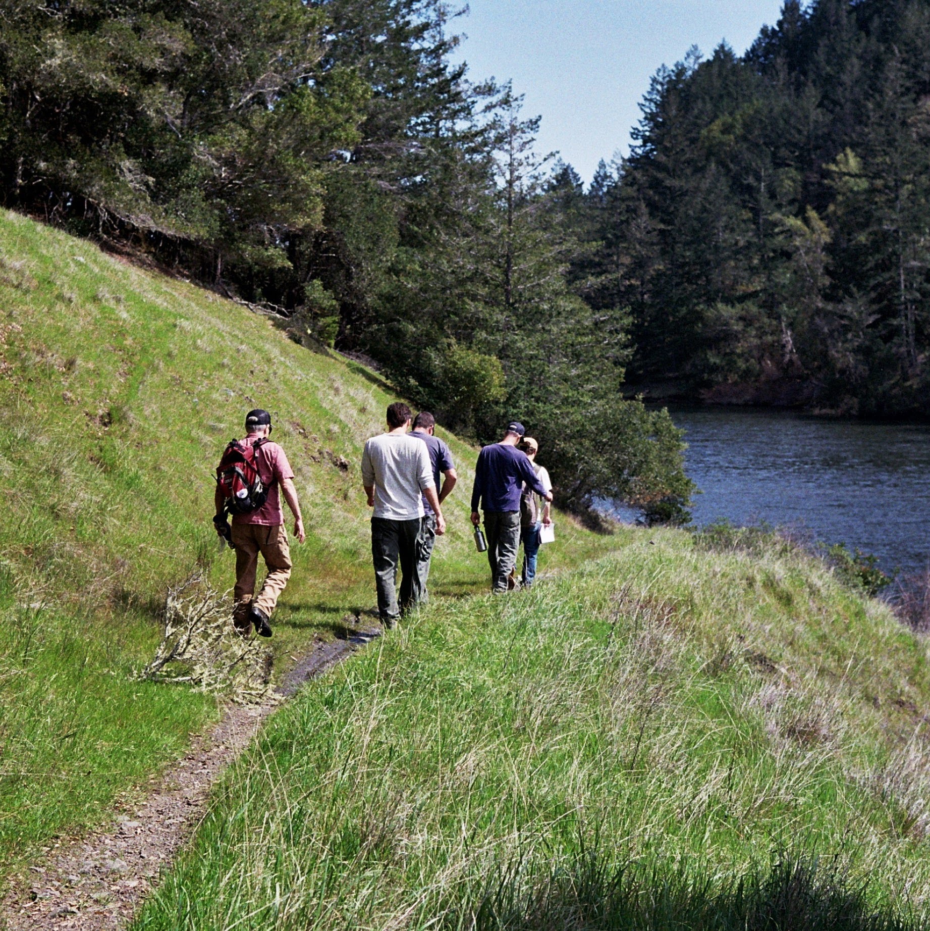 Group walking along narrow dirt trail beside reservoir in Marin Water watershed