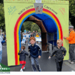 Community event with families and cyclists passing through rainbow-themed Alto Tunnel display supporting North-South Greenway.