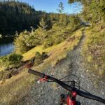 View from bike handlebars along narrow dirt path beside reservoir in Mt. Tam Watershed.
