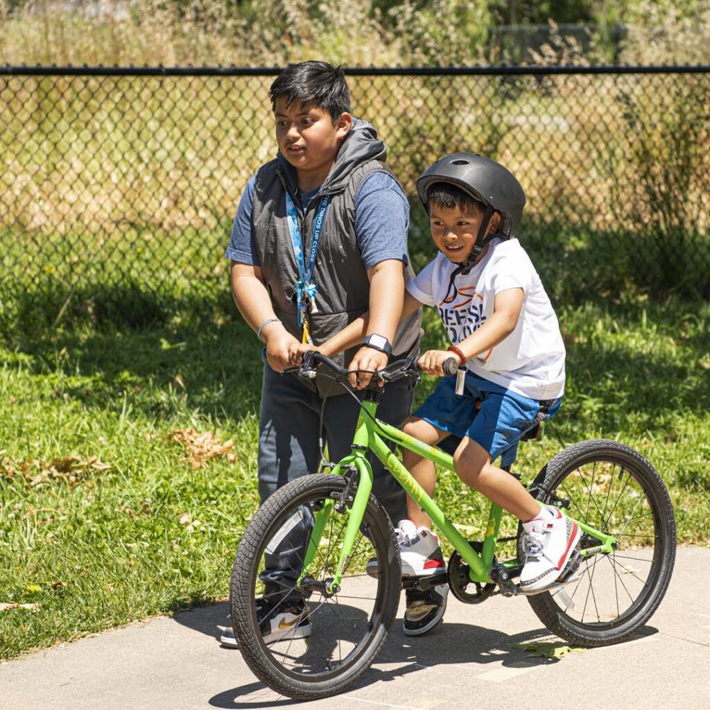 Little boy learning to ride with help of older boy at Bikefest