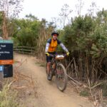 Cyclist riding past trailhead sign marking Dias Ridge Trail with connections to Miwok Trail and Panoramic Highway